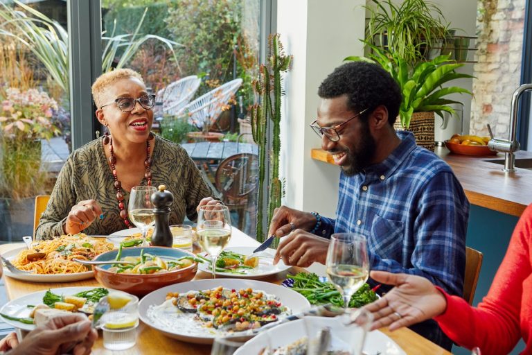 Extended family sitting at dining table at gathering enjoying home cooked meal talking and laughing, togetherness, healthy eating, meal time, socialising