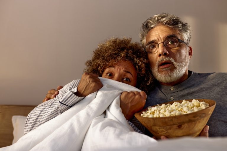 Mature couple watching a horror movie on TV in the bedroom.