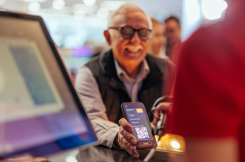 A senior Caucasian man is at the cash register in the cinema, paying with his online mobile app for the tickets.
