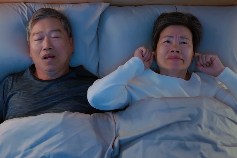Asian senior couple in bed - husband snoring while sleeping and wife cannot sleep feeling irritable