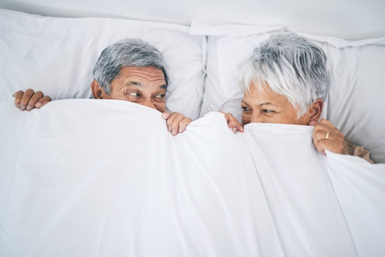 senior couple covering with a blanket in a bedroom