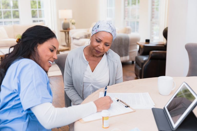 Nurse documents the senior patient's concerns at home. Tablet computer and paper forms.