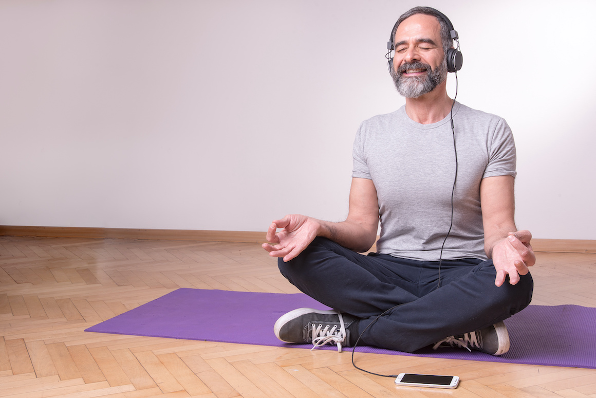 Senior older man practicing yoga and listening to his favourite relaxation music