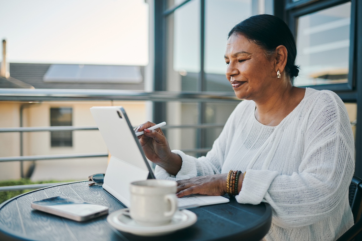 A mature woman focuses on her tablet while seated at an outdoor patio table