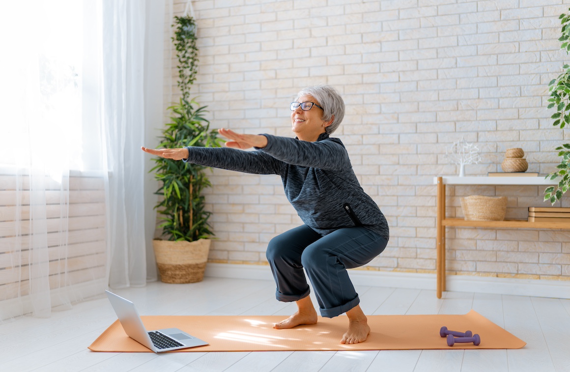 Senior woman in activewear watching online courses on laptop while exercising at home.