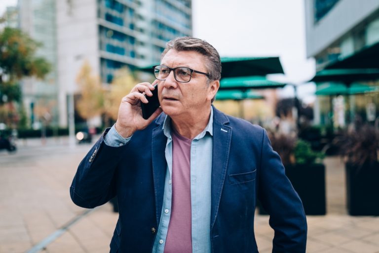 Senior man looks worried as he talks on his mobile phone in the street