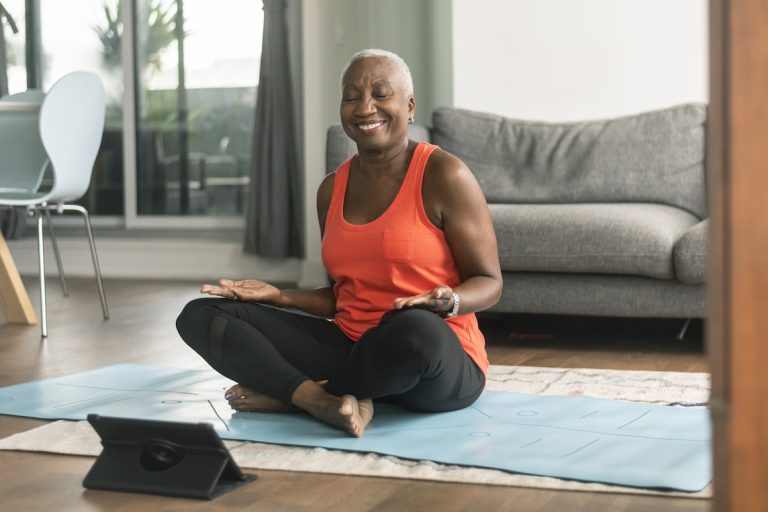 A senior Black woman participates in a virtual fitness class from hotel room